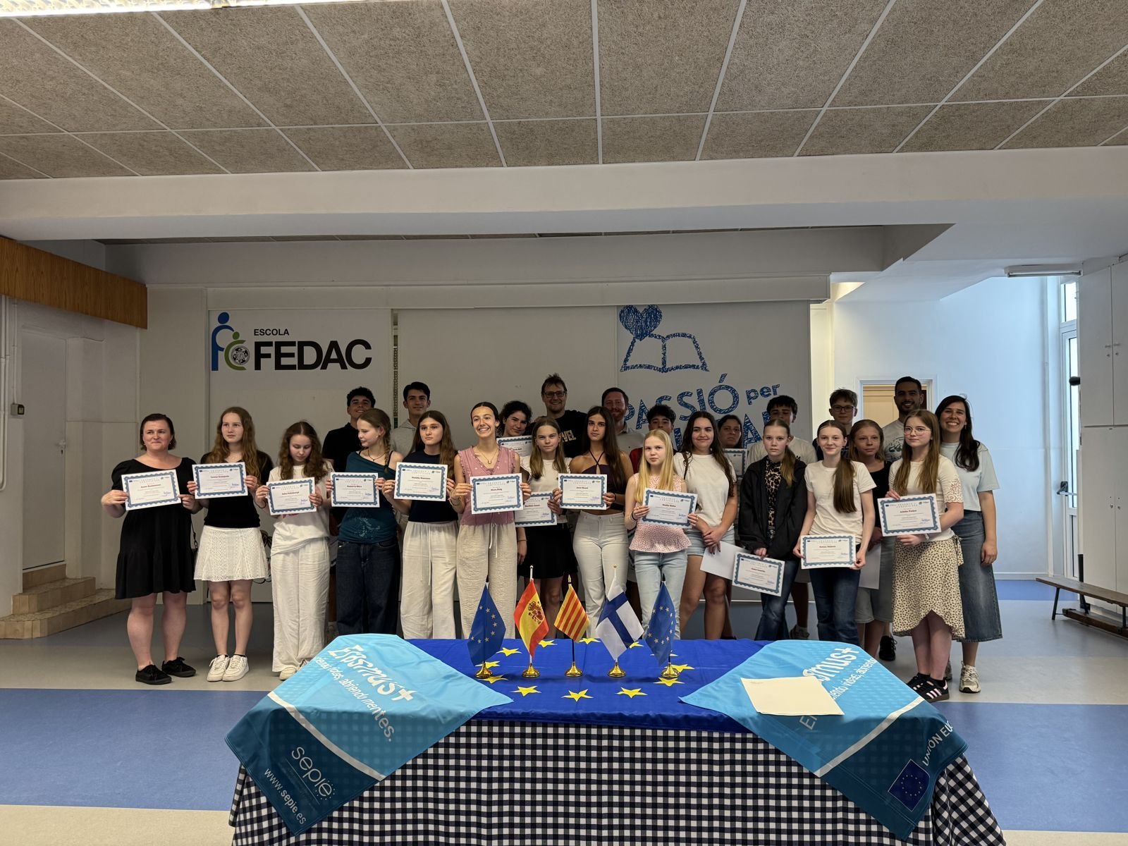 Alumnes amb els certificats Erasmus+ davant les banderes europees a l'escola FEDAC Sant Andreu