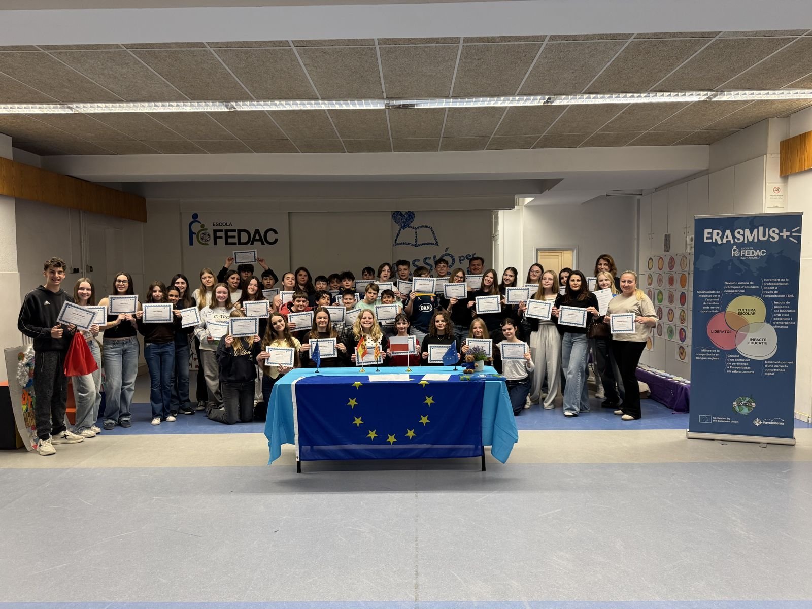 Alumnes i docents amb els certificats Erasmus+ i la bandera europea a l'escola FEDAC Sant Andreu