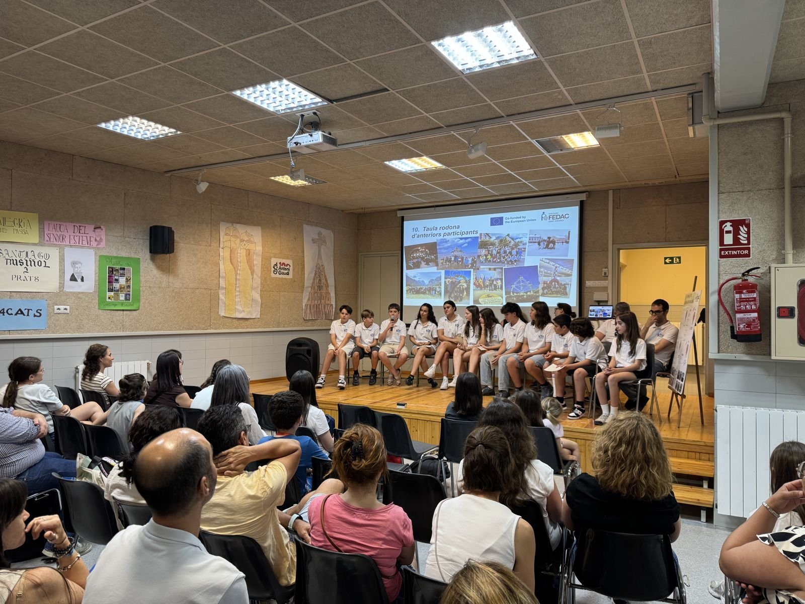 Taula rodona d'antics participants Erasmus+ davant de famílies i alumnes a la sala d'actes de l'escola